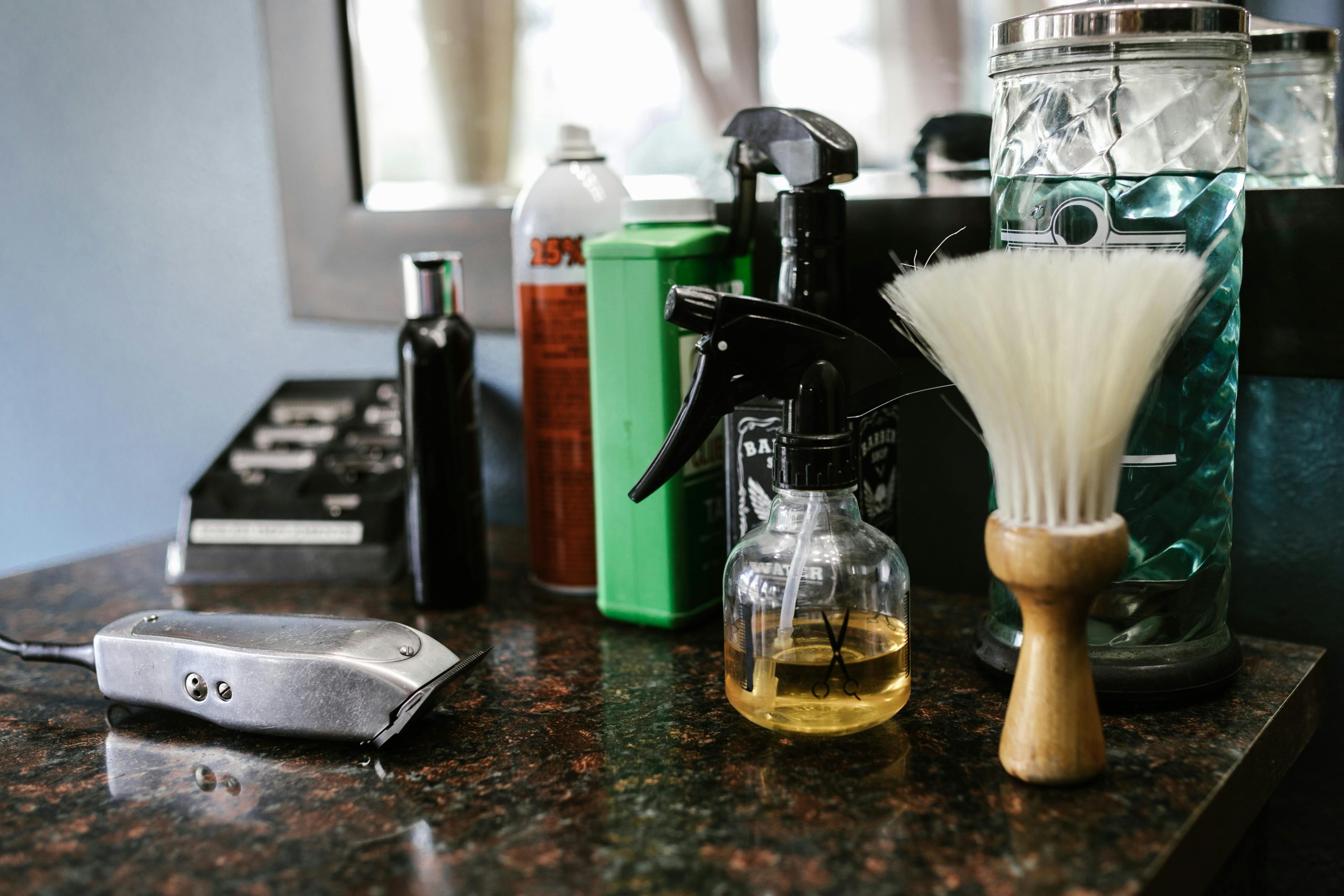 Close-up of barber tools on counter including clippers, spray bottle, and brush in a stylish barbershop.